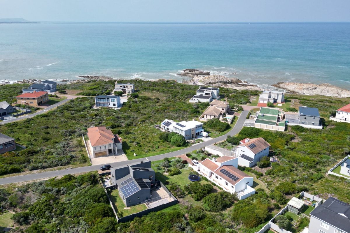 An aerial view of a coastal residential estate featuring multiple homes, paved roads, and proximity to the ocean.
