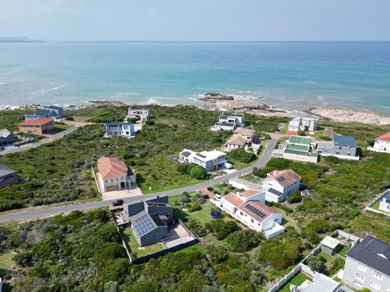 An aerial view of a coastal residential estate featuring multiple homes, paved roads, and proximity to the ocean.