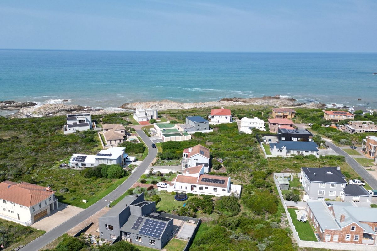 An aerial view of a coastal residential neighborhood featuring various homes, paved streets, and direct proximity to the ocean.