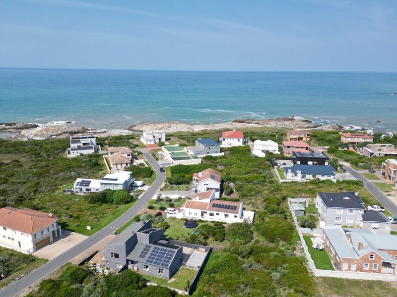An aerial view of a coastal residential neighborhood featuring various homes, paved streets, and direct proximity to the ocean.
