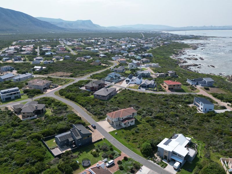 An aerial view of a coastal residential neighborhood featuring established homes, paved roads, and proximity to the ocean and natural landscape.