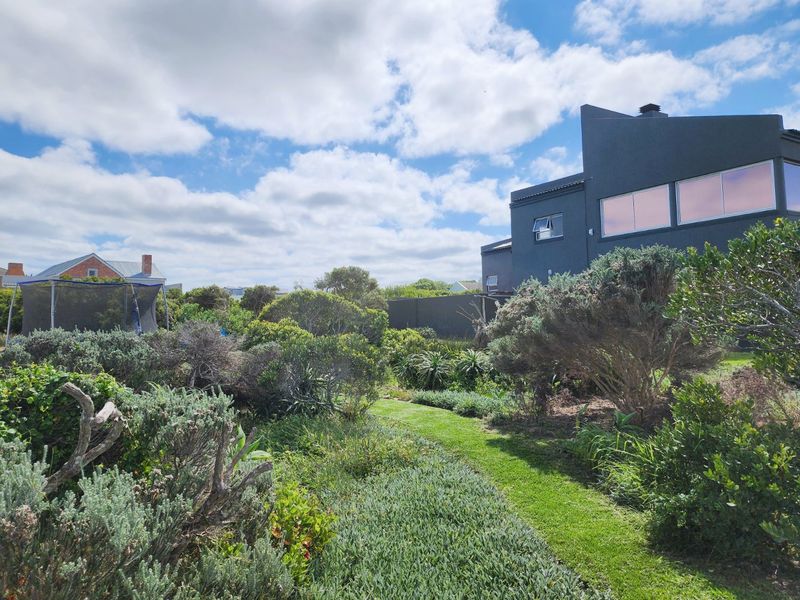 A well-maintained residential garden featuring established shrubbery and a manicured lawn area adjacent to a modern dark-toned dwelling.