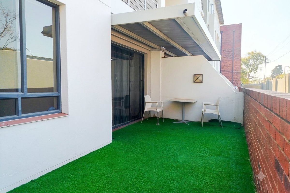 A private ground-floor patio area featuring artificial grass, a fixed overhead awning, and a brick boundary wall, providing a low-maintenance outdoor space.
