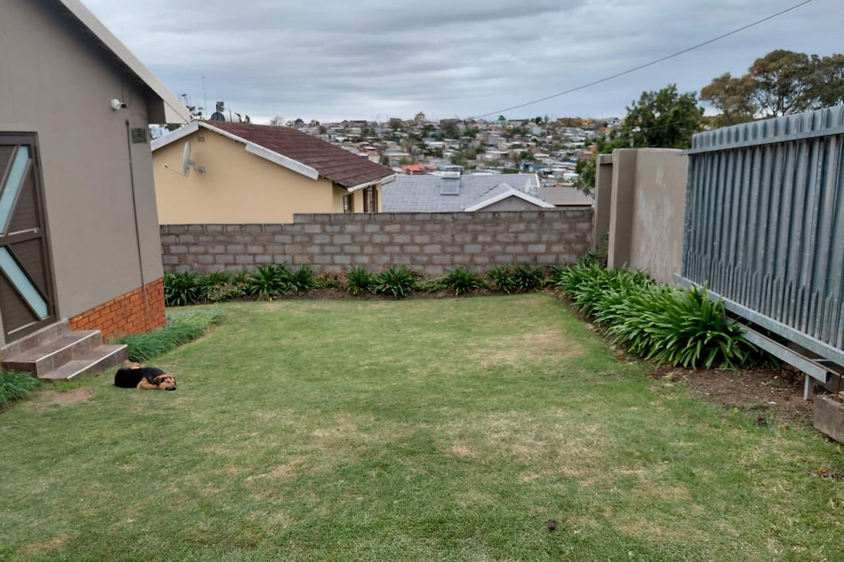 A private rear garden featuring a lawn, landscaped garden beds, and a secure boundary wall with metal fencing.