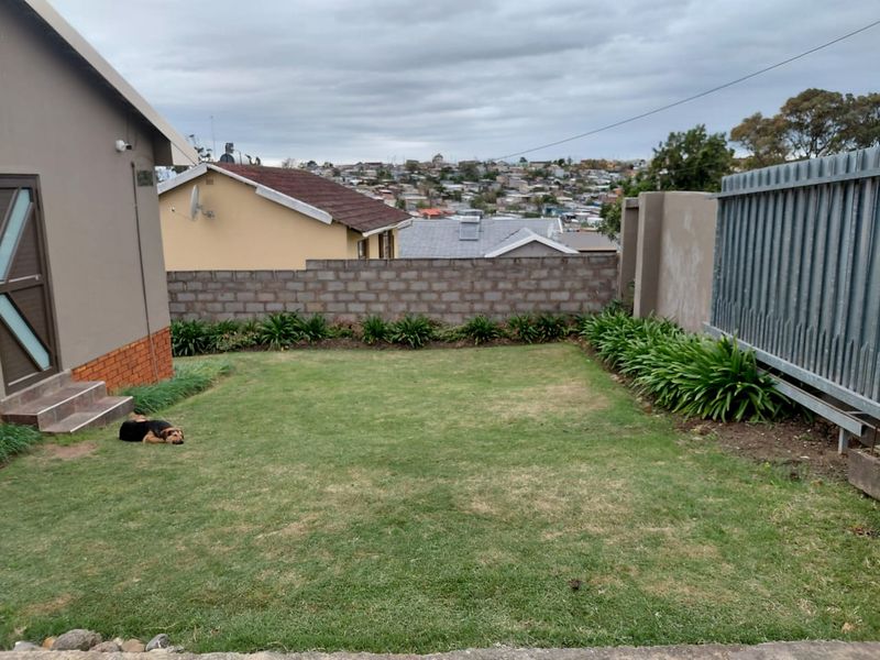 A private rear garden featuring a lawn, landscaped garden beds, and a secure boundary wall with metal fencing.