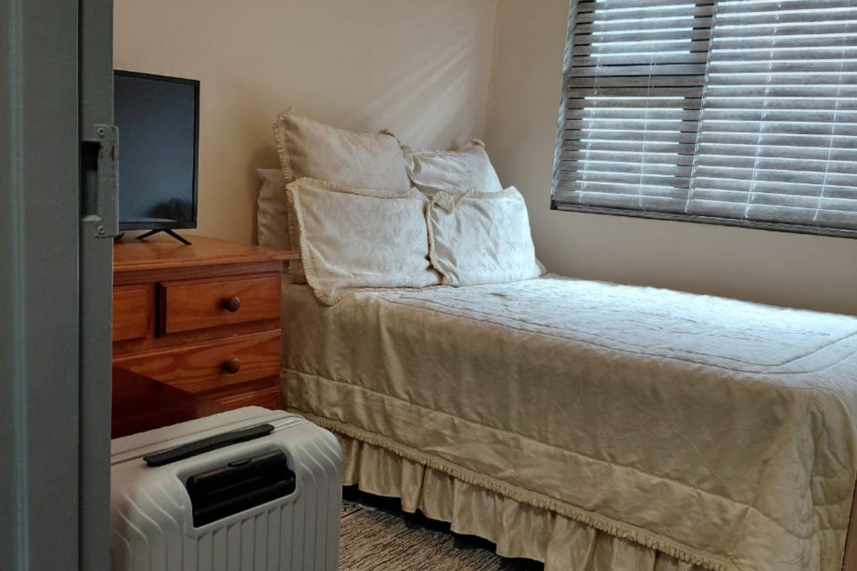 A compact bedroom featuring laminate flooring, neutral wall tones, and a window fitted with venetian blinds.