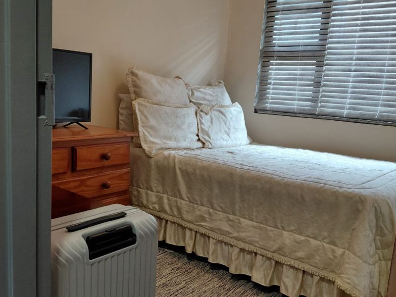 A compact bedroom featuring laminate flooring, neutral wall tones, and a window fitted with venetian blinds.