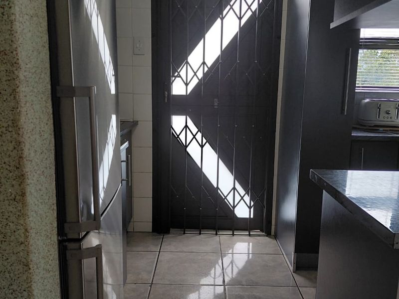 A functional kitchen area featuring tiled flooring, built-in cabinetry, and a secure metal gate leading to the exterior.