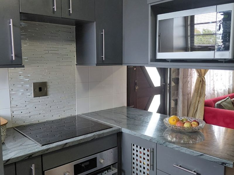 Modern kitchen featuring dark grey cabinetry, stone countertops, integrated electric hob, built-in oven, and a built-in microwave.