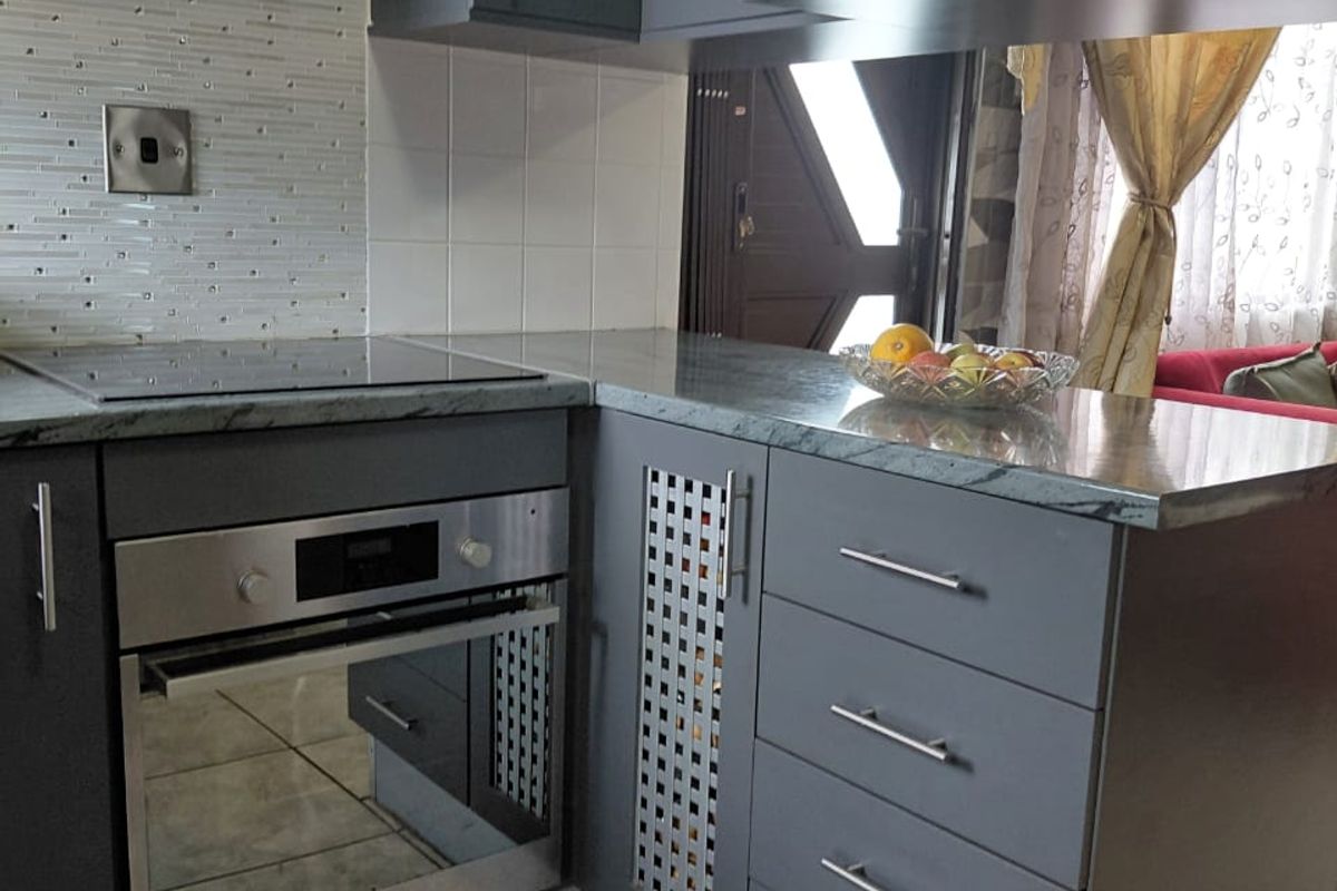Modern kitchen featuring dark grey cabinetry, built-in oven, electric hob, integrated microwave, and a decorative mosaic tile backsplash.