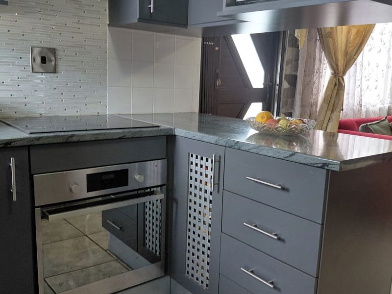 Modern kitchen featuring dark grey cabinetry, built-in oven, electric hob, integrated microwave, and a decorative mosaic tile backsplash.