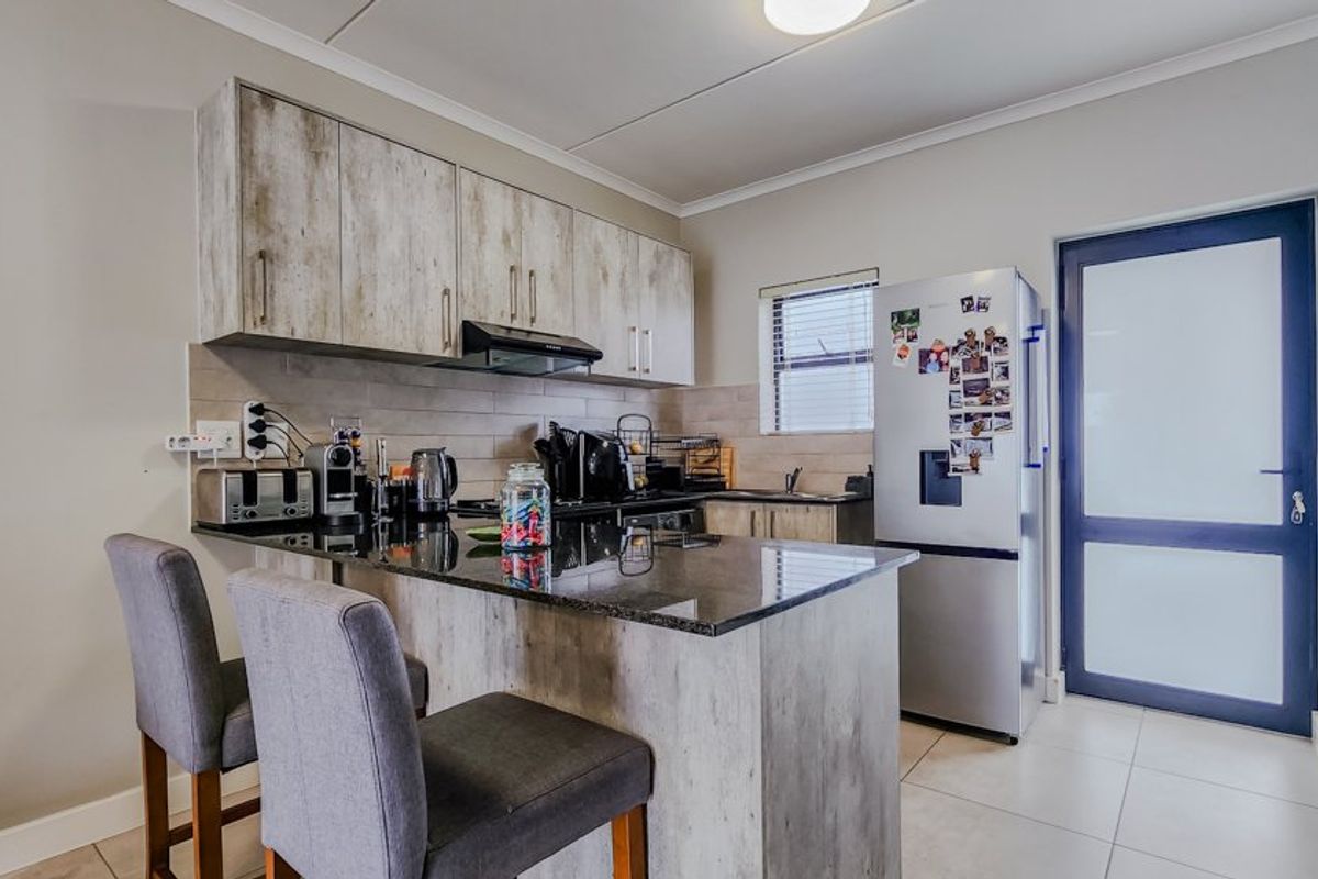 Modern kitchen featuring granite countertops, ample built-in cabinetry, a tiled backsplash, and a breakfast bar area with direct access to the exterior.