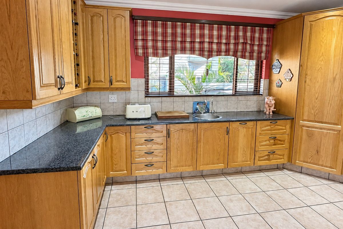 A functional kitchen featuring traditional oak cabinetry, dark granite countertops, tiled flooring, and a window overlooking the exterior.