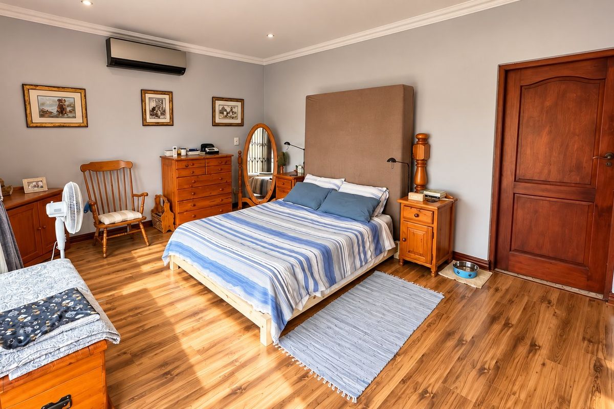 A well-maintained bedroom featuring warm laminate flooring, crown molding, and a wall-mounted air conditioning unit.