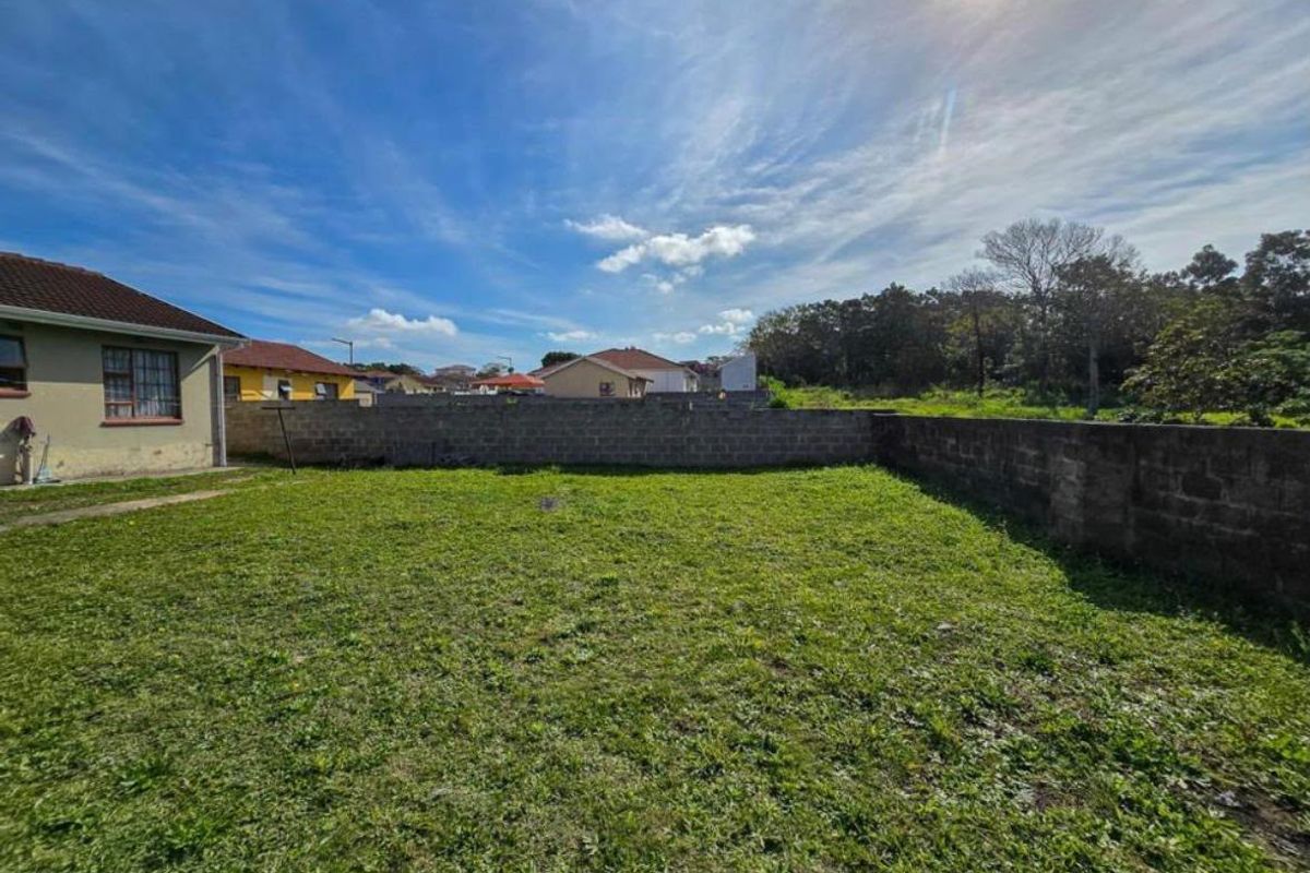 A spacious rear garden area featuring a large lawn and concrete block boundary walls, offering potential for landscaping and outdoor development.
