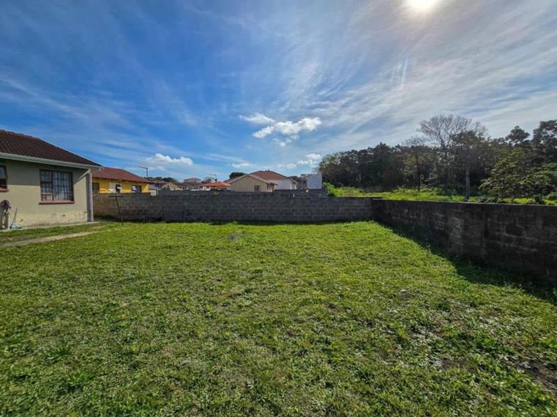 A spacious rear garden area featuring a large lawn and concrete block boundary walls, offering potential for landscaping and outdoor development.