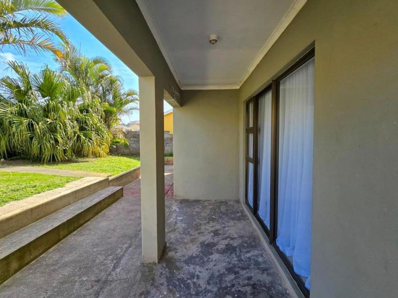 A covered concrete patio area featuring sliding glass doors and direct access to the garden, offering a functional outdoor space for relaxation.