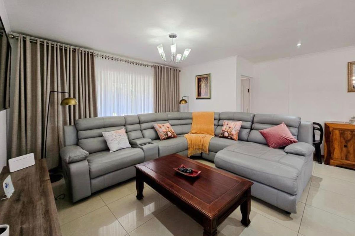 A well-maintained living room featuring neutral tiled flooring, modern lighting fixtures, and large windows with floor-to-ceiling curtains.