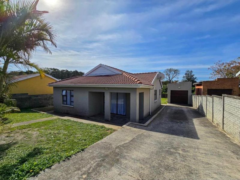 Front view of a single-story house featuring a tiled roof, covered entrance, concrete driveway, and a detached garage with a surrounding boundary wall.