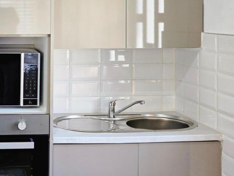A compact kitchen area featuring fitted cabinetry, a stainless steel sink with mixer tap, subway tile backsplash, and built-in oven and microwave.