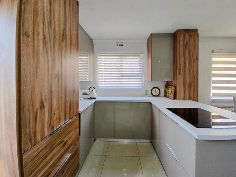 Modern kitchen featuring wood-grain and neutral cabinetry, stone countertops, an integrated electric hob, and tiled flooring with ample natural light.