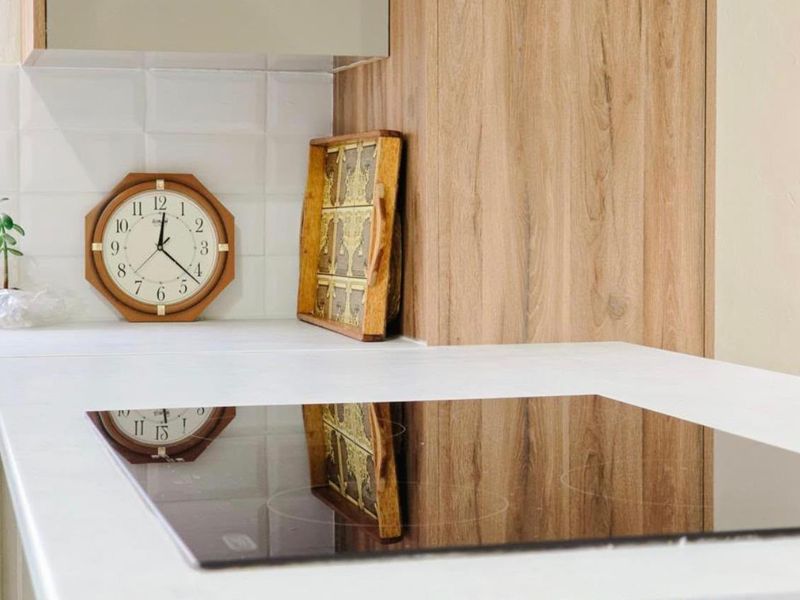 A modern kitchen featuring a sleek induction hob, light wood-grain cabinetry, and a clean white subway tile backsplash.