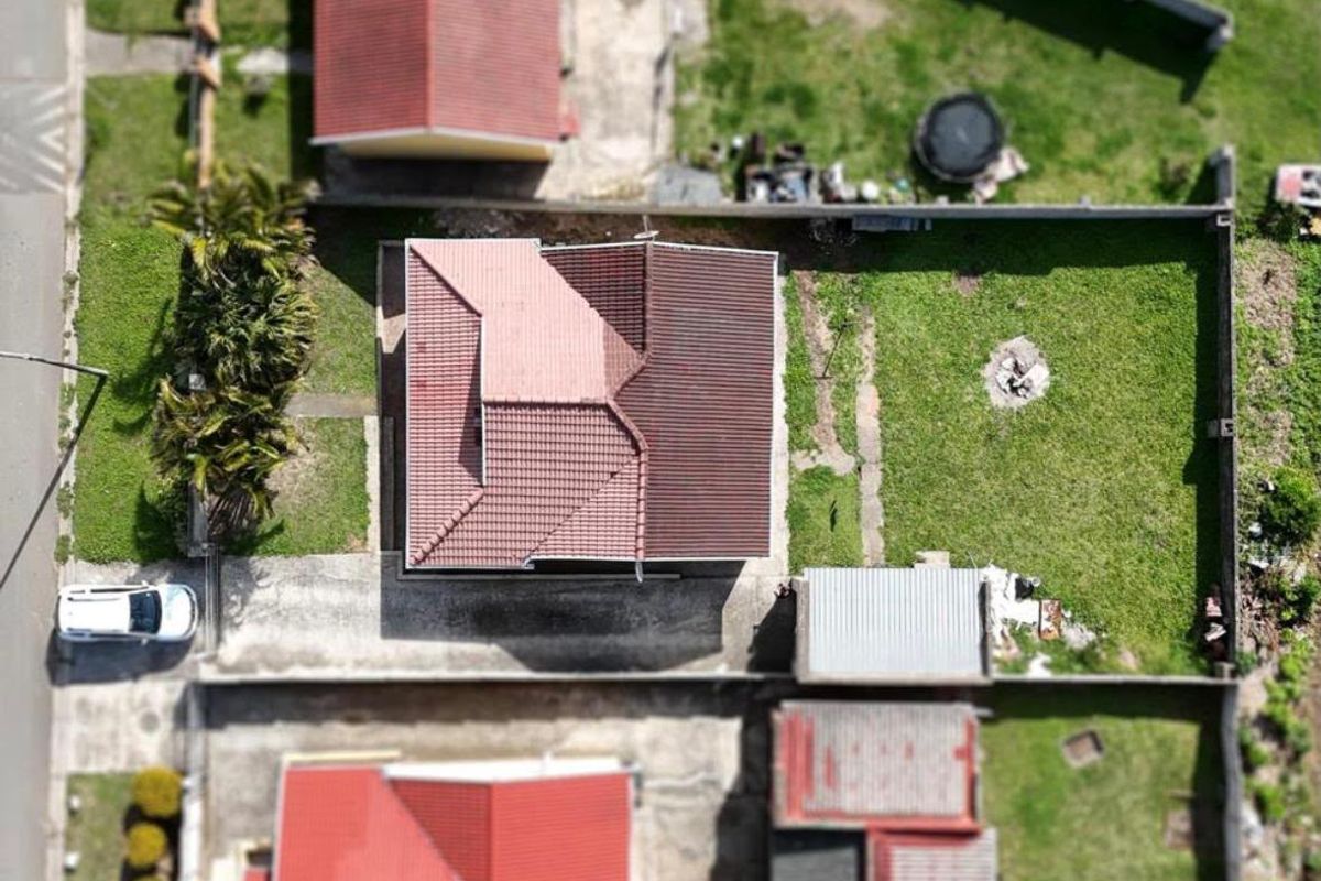Aerial view of the property showing the house footprint, tiled roof, surrounding garden, boundary walls, and driveway access.