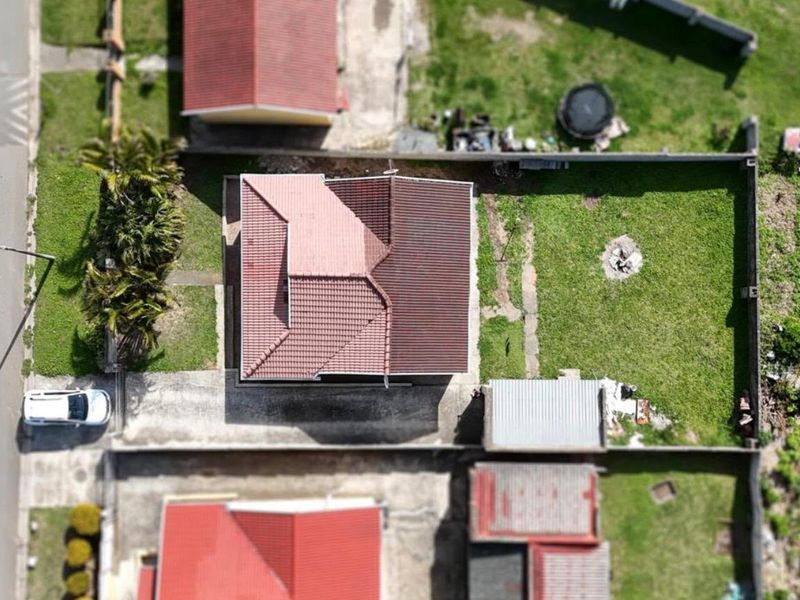 Aerial view of the property showing the house footprint, tiled roof, surrounding garden, boundary walls, and driveway access.