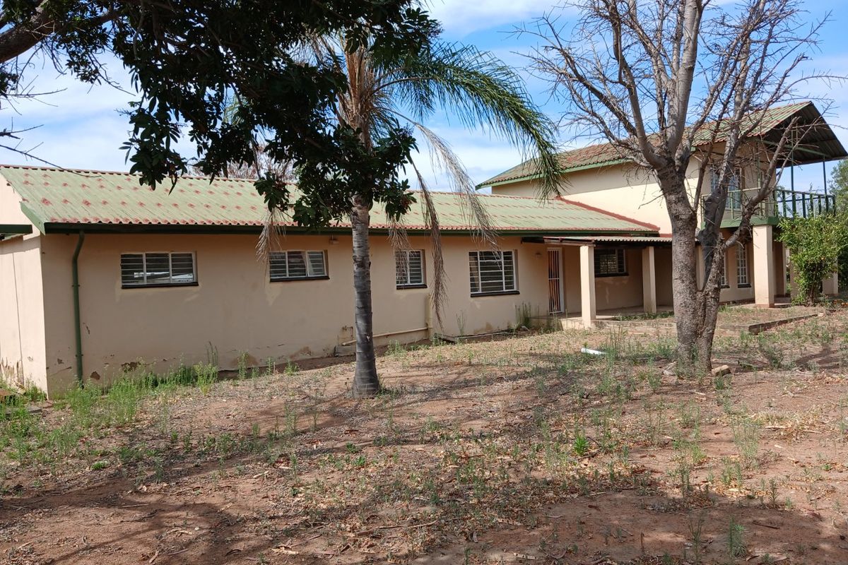 Rear view of a farm-style dwelling featuring a metal roof, covered patio, and balcony, set within an expansive, unlandscaped garden area.