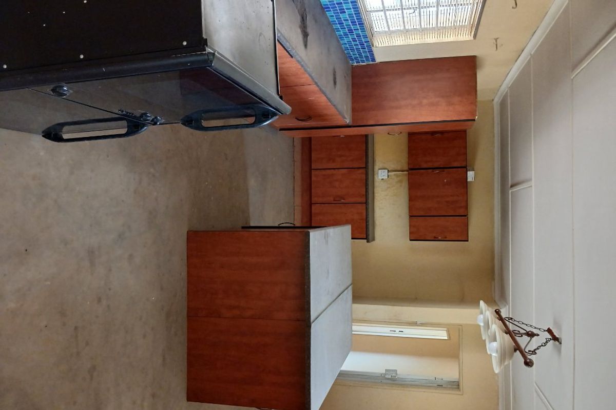 A dated kitchen featuring wooden cabinetry, laminate countertops, and a mosaic tile backsplash, requiring cosmetic updates to modernize the space.