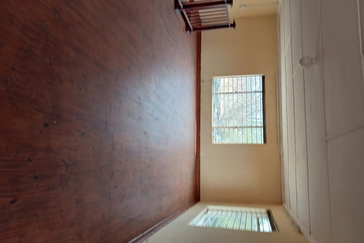 An empty bedroom featuring timber flooring and security bars on the windows, offering a blank canvas for renovation.