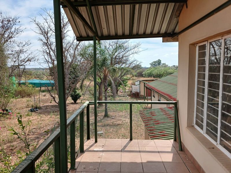 An elevated outdoor balcony featuring tiled flooring, a metal roof covering, and security-barred windows, overlooking the farm grounds.