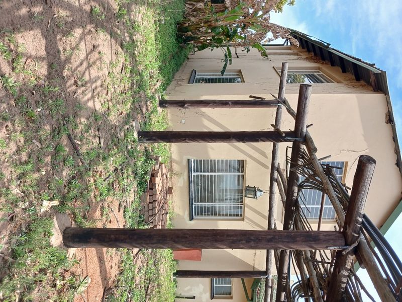 Rear exterior view of the farm property featuring a timber pergola structure, security-fitted windows, and weathered exterior wall finishes.