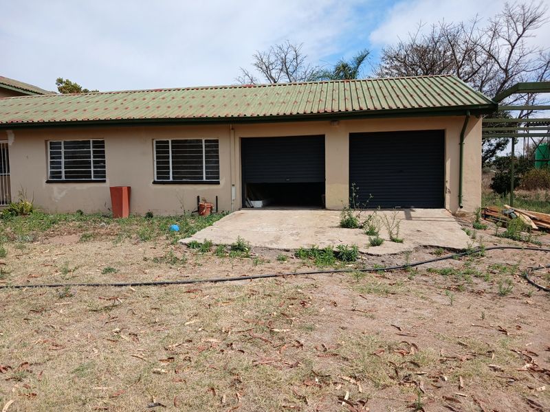 Exterior view of a double garage featuring roller shutter doors and a corrugated metal roof, set on a rural property with a concrete apron.