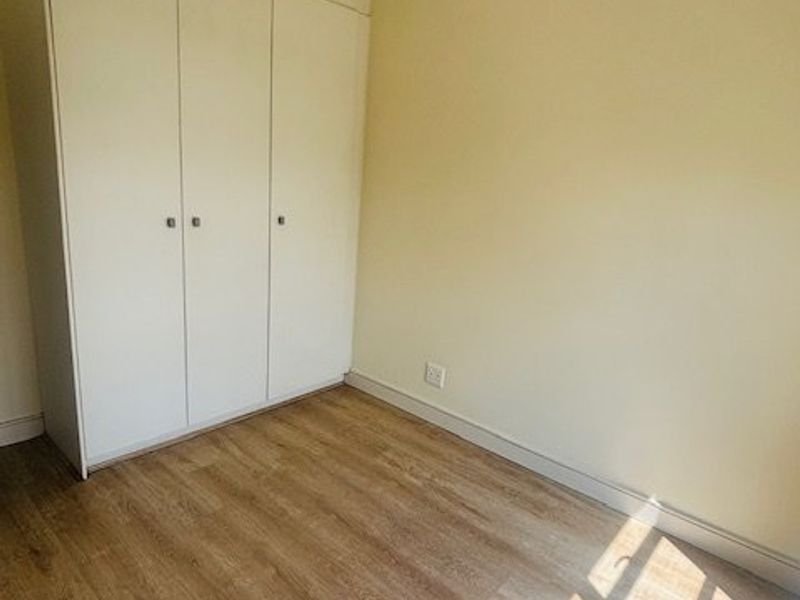 A bright, empty bedroom featuring modern laminate flooring and a clean, white built-in wardrobe with ample storage space.