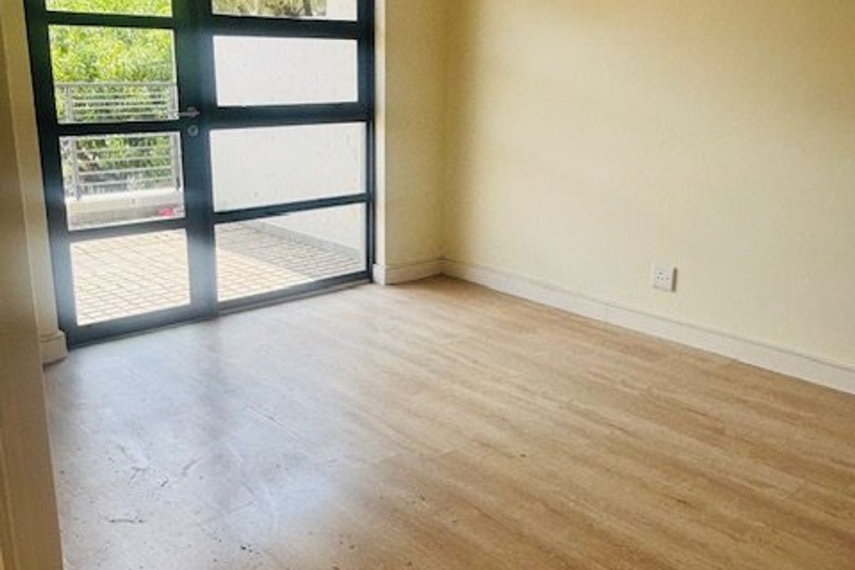 An empty living room featuring light-toned laminate flooring and black-framed glass double doors providing access to an outdoor area.