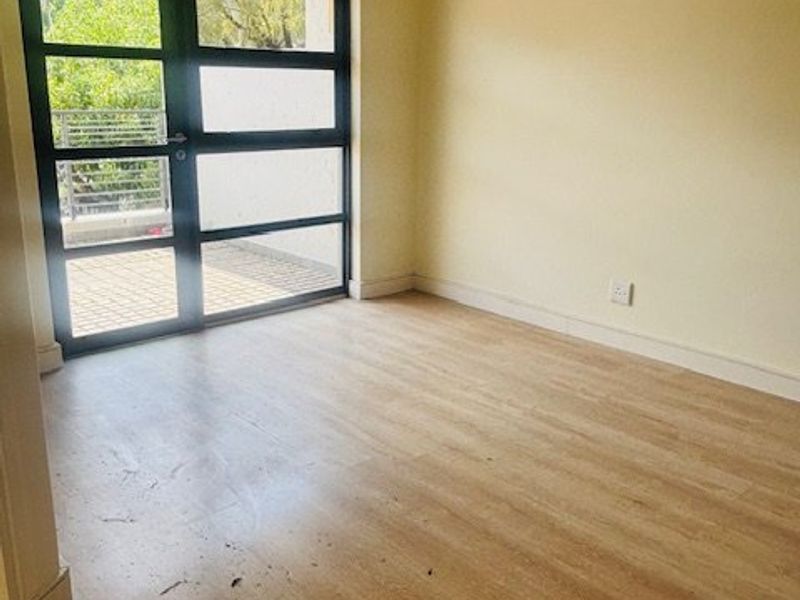 An empty living room featuring light-toned laminate flooring and black-framed glass double doors providing access to an outdoor area.