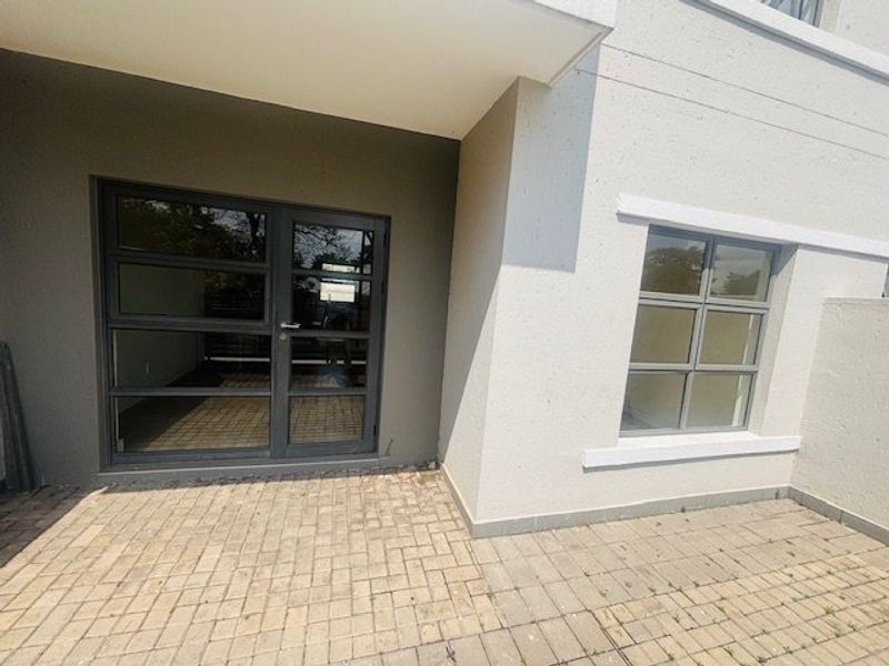 A clean, paved patio area featuring modern aluminium-framed glass doors and windows, providing a functional outdoor space for the apartment.