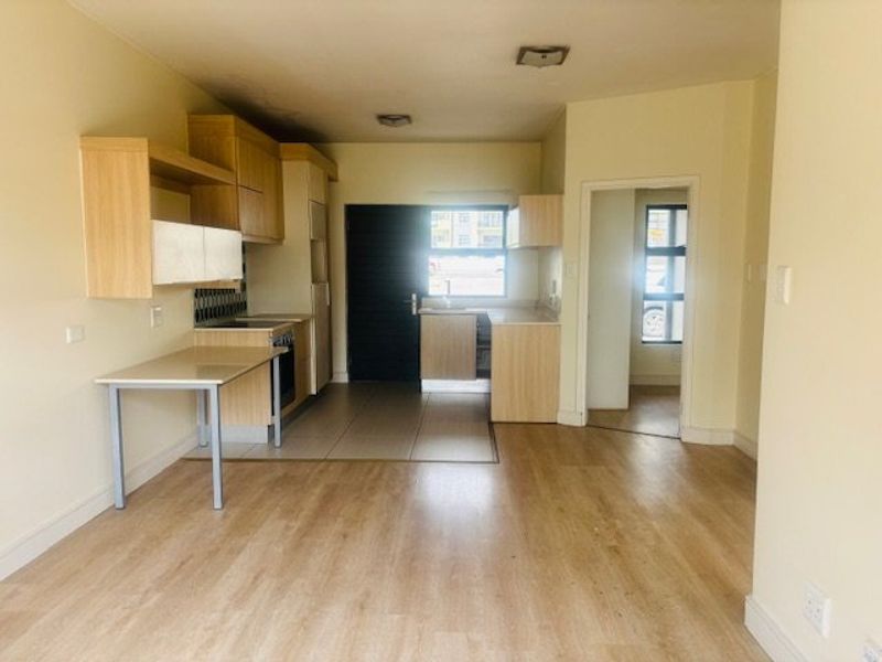 Open plan living area featuring a functional kitchen with built-in cabinetry, oven, and hob, leading to a bright, tiled kitchen space and laminate flooring.