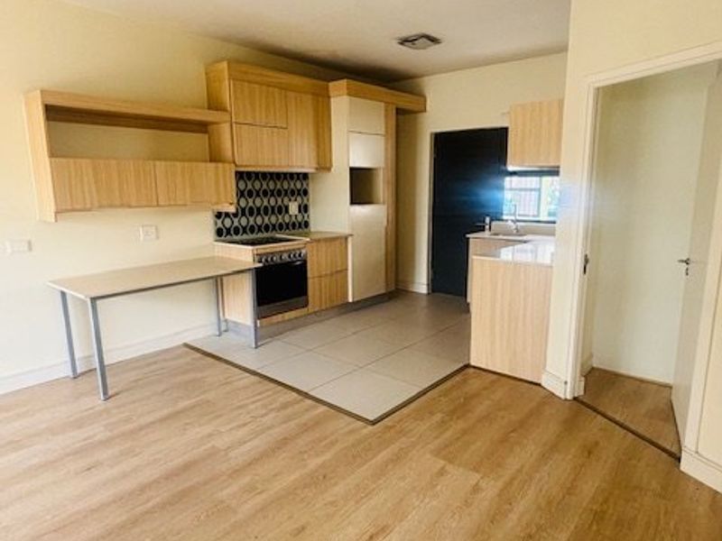 An open-plan kitchen and living area featuring light wood-look laminate flooring, modern cabinetry, a built-in stove, and a decorative tiled backsplash.