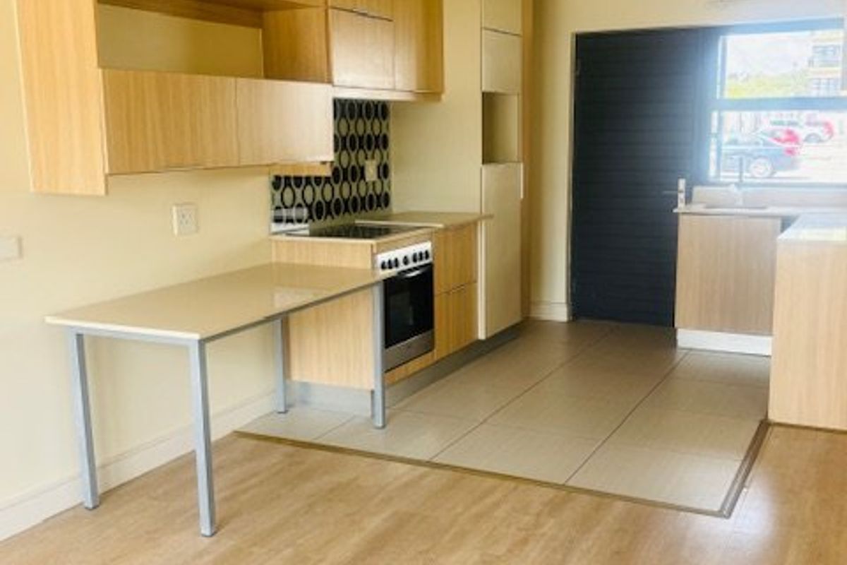 A functional kitchen featuring light wood-tone cabinetry, built-in oven and hob, tiled splashback, and a convenient integrated breakfast bar area.