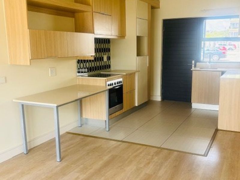 A functional kitchen featuring light wood-tone cabinetry, built-in oven and hob, tiled splashback, and a convenient integrated breakfast bar area.