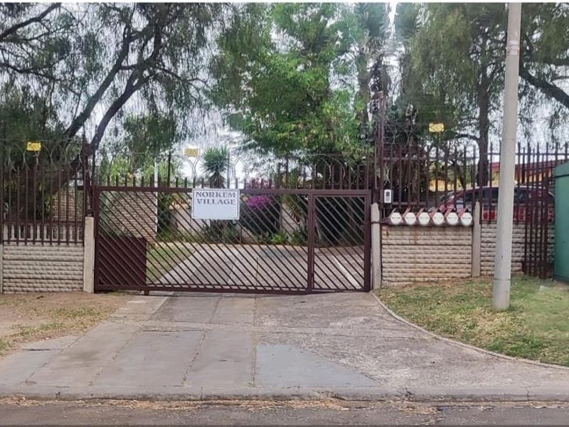 Front entrance view of Norkem Village featuring a secure gated access point, perimeter fencing, and a concrete driveway.