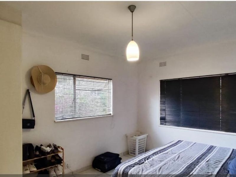 A functional bedroom featuring built-in wardrobe storage, dual windows with venetian blinds, and a central pendant light fixture.