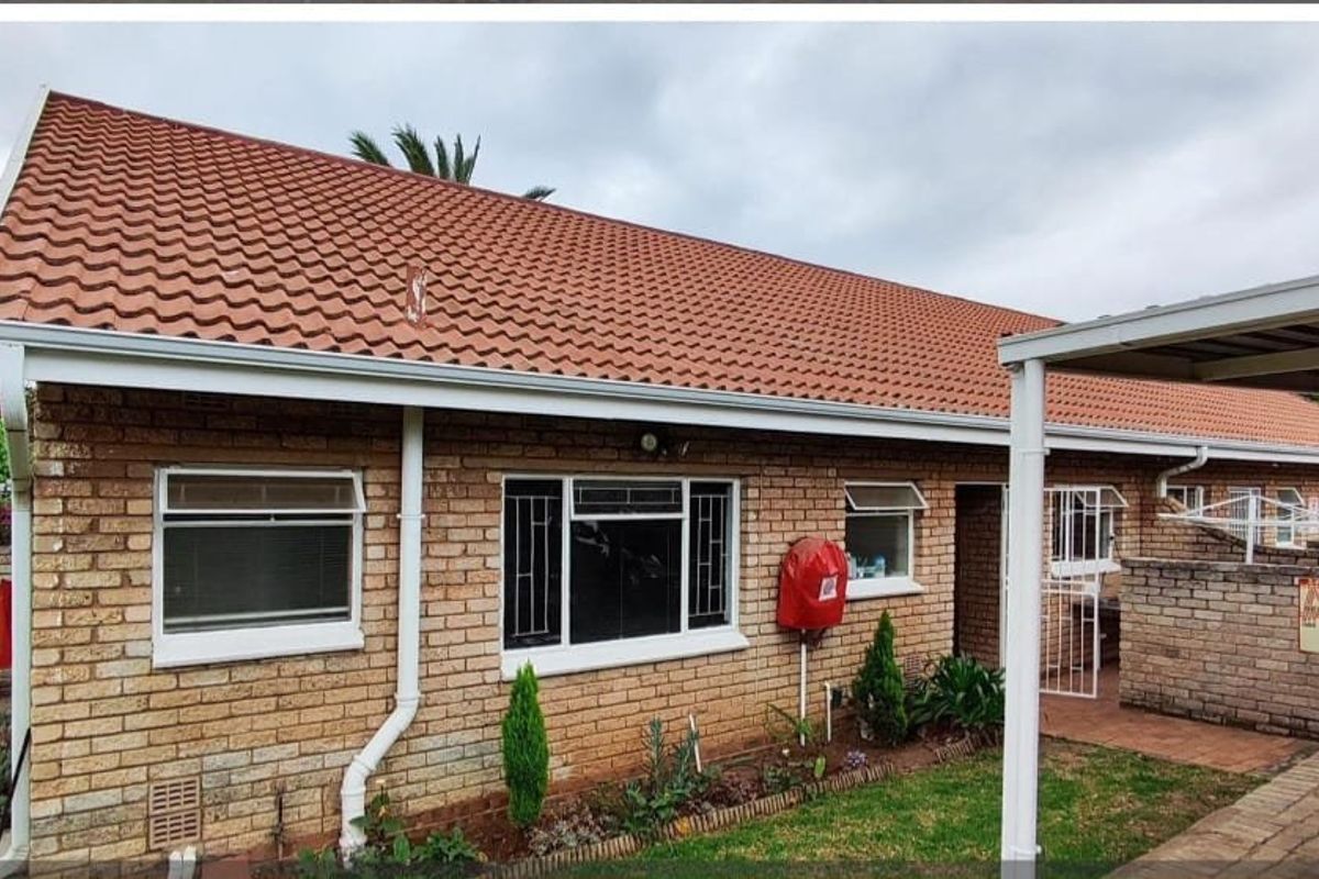 Rear view of a face brick house featuring a tiled roof, security gates, and an attached carport area.