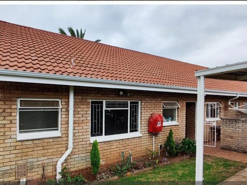Rear view of a face brick house featuring a tiled roof, security gates, and an attached carport area.