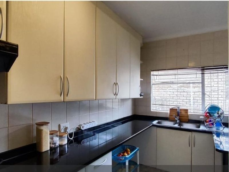 A functional kitchen featuring ample built-in cabinetry, black granite countertops, a double basin sink, and a tiled backsplash.