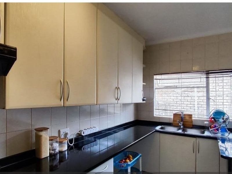 A functional kitchen featuring light-toned cabinetry, contrasting black granite countertops, a stainless steel sink, and a tiled backsplash.