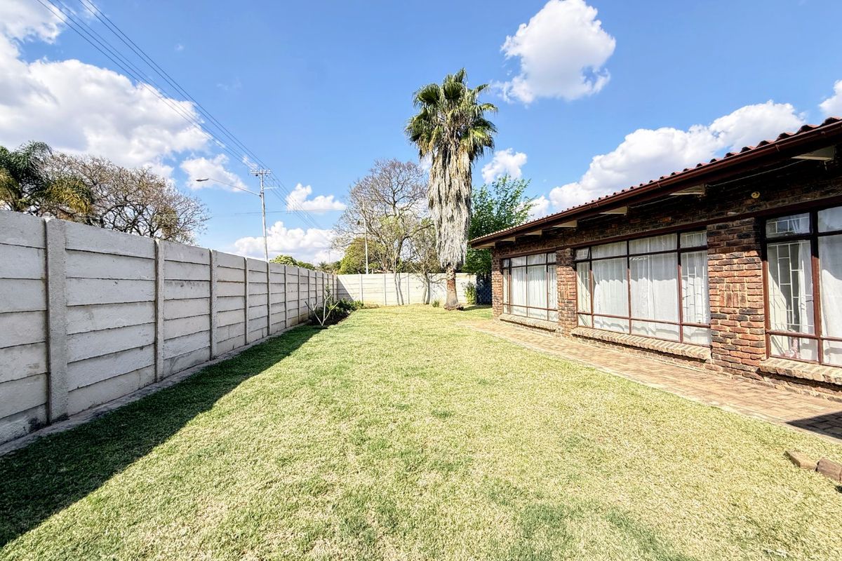 A spacious rear garden featuring a well-maintained lawn, a paved walkway, and a brick-faced exterior wall with large windows.