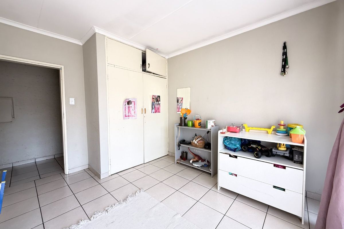 A bedroom featuring ceramic floor tiles, a built-in wardrobe with overhead storage, and neutral wall finishes.